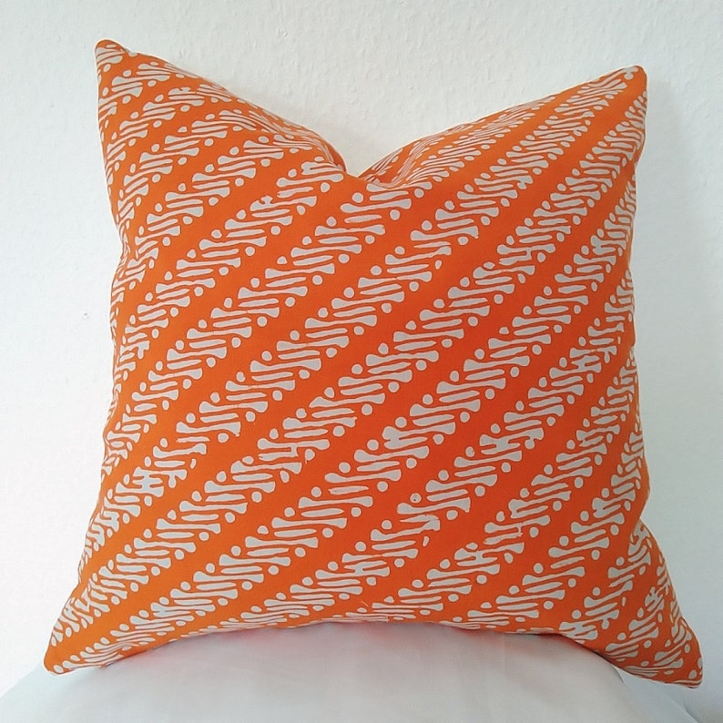 May include: Orange cushion with a white geometric pattern. The pattern is a series of diagonal lines with small white circles.