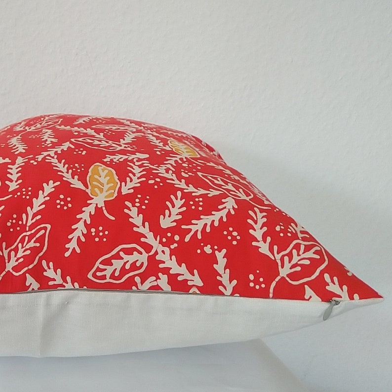 Pu&ograve; includere: Cuscino rosso con un motivo floreale bianco e giallo. Il cuscino ha un bordo bianco e una cerniera.