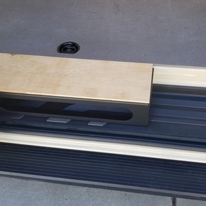 May include: A wooden shelf with a black frame and a rectangular cutout. The shelf is mounted to the side of a vehicle.