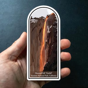 May include: A rectangular sticker featuring an illustration of Horsetail Fall in Yosemite National Park, California. The image shows a waterfall with an orange glow, resembling fire, cascading down a dark rock face. The sticker has a white border.