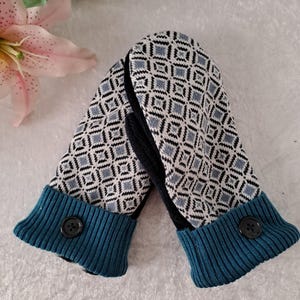 May include: Knitted mittens with a diamond pattern in grey and white. The cuffs are teal with a black button detail. These mittens are designed for warmth and style, perfect for cold weather.
