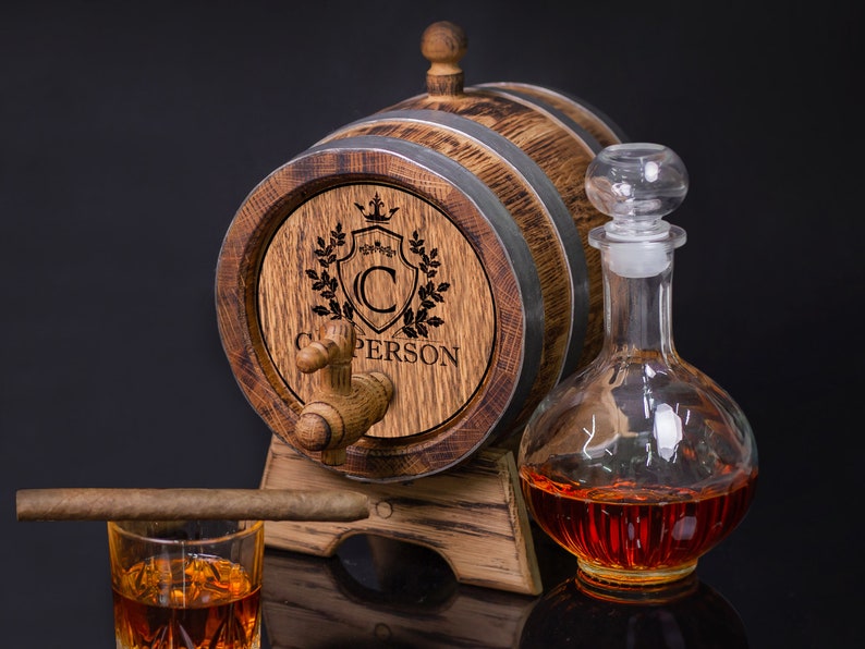May include: A wooden barrel with a metal band and a spigot, engraved with a crest and the name "C. PERSON". The barrel is on a stand and has a clear glass decanter with a stopper filled with amber liquid.