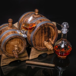 May include: Two wooden barrels with metal bands, one with a glass of amber liquid inside, and a glass decanter filled with amber liquid. The barrels are on wooden stands and there is a brown cigar on the table.