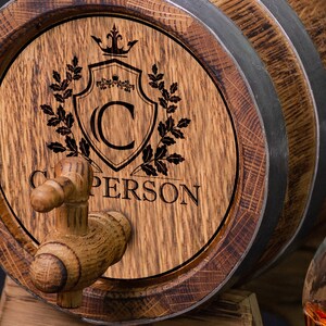 May include: A wooden barrel with a spigot and a personalized inscription. The inscription includes a crown, a shield with the letter "C", and the name "C. PERSON".
