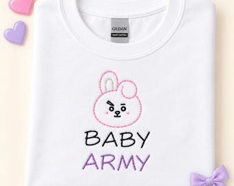 May include: A white crew neck t-shirt featuring an embroidered pink bunny character face above the black text BABY and the purple text ARMY. The shirt has a Gildan brand label at the neck and a small purple bow attached to the bottom right corner.