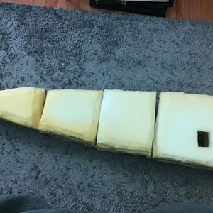 May include: A series of foam blocks in varying shapes and shades of yellow and white. The blocks are arranged in a row, with one block having a square cut-out. The blocks are sitting on a gray surface.