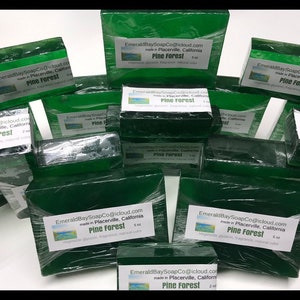 May include: A collection of green Pine Forest soap bars, wrapped in clear plastic. Each bar has a white label with the text "EmeraldBaySoapCo@icloud.com" and "Pine Forest". The soap is made with vegetable glycerin, fragrance, and natural color.