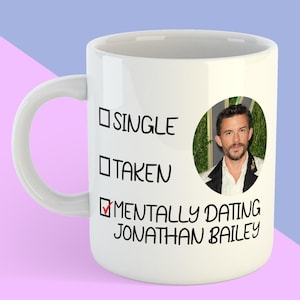 May include: White ceramic mug with a black and white graphic that reads "Single, Taken, Mentally Dating Jonathan Bailey". A checkmark is next to "Mentally Dating" and a photo of Jonathan Bailey is in the background.