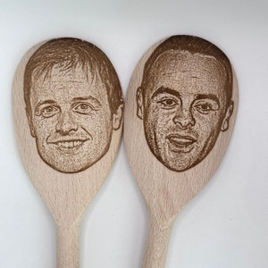 以下が含まれることがあります： 男性の顔がレーザー彫刻された木製のスプーン2本。スプーンは茶色で、自然な木製の仕上げです。