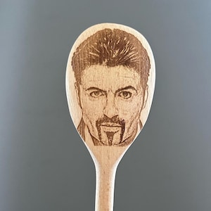 May include: A wooden spoon with a laser-engraved image of a man's face. The man has dark hair, a moustache, and a goatee.