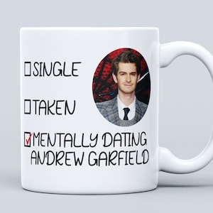Puede incluir: Taza de cerámica blanca con un gráfico en blanco y negro que dice "Soltero, En Pareja, Mentalmente Saliendo con Andrew Garfield" con una marca de verificación junto a la última opción. Una foto de Andrew Garfield está en un círculo en la taza.