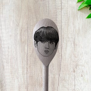 Puede incluir: Una cuchara de madera con una imagen grabada en blanco y negro de una cara.