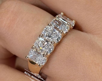 May include: A gold ring featuring five rectangular radiant-cut clear stones arranged in a row. The band is polished yellow gold. The text RING MOISSANITE is printed in white on the lower portion of the band, accompanied by a decorative flourish.