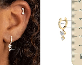 May include: Gold-toned earrings with clear gemstones. One earring is a hoop with a dangling gemstone cluster. The other earring is a stud with a teardrop-shaped gemstone. The hoop earring measures 8 mm in diameter.