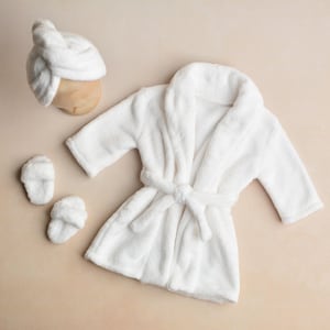 May include: A white plush robe with a matching headband and slippers. The robe has a tie belt and long sleeves.