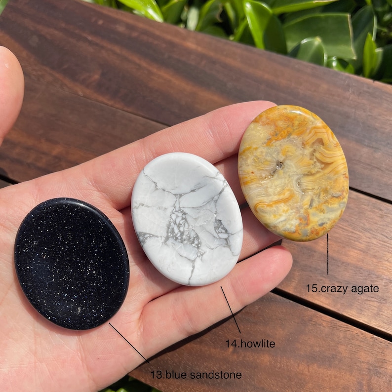 May include: Three oval-shaped polished stones, one black, one white with gray veins, and one yellow with brown veins. The stones are labeled "13. blue sandstone", "14. howlite", and "15. crazy agate".