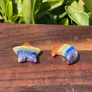 May include: Two small, multi-colored, layered stone carvings. One is shaped like a star and the other is shaped like a crescent moon. Both are made of seven different colors of stone, including red, orange, yellow, green, blue, indigo, and purple.