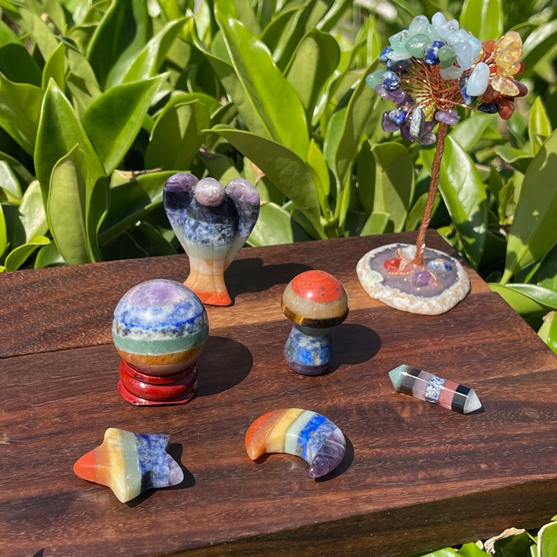 May include: Seven chakra crystal figurines, including a sphere, angel, mushroom, crescent moon, star, and a wand. The crystals are arranged on a wooden surface.