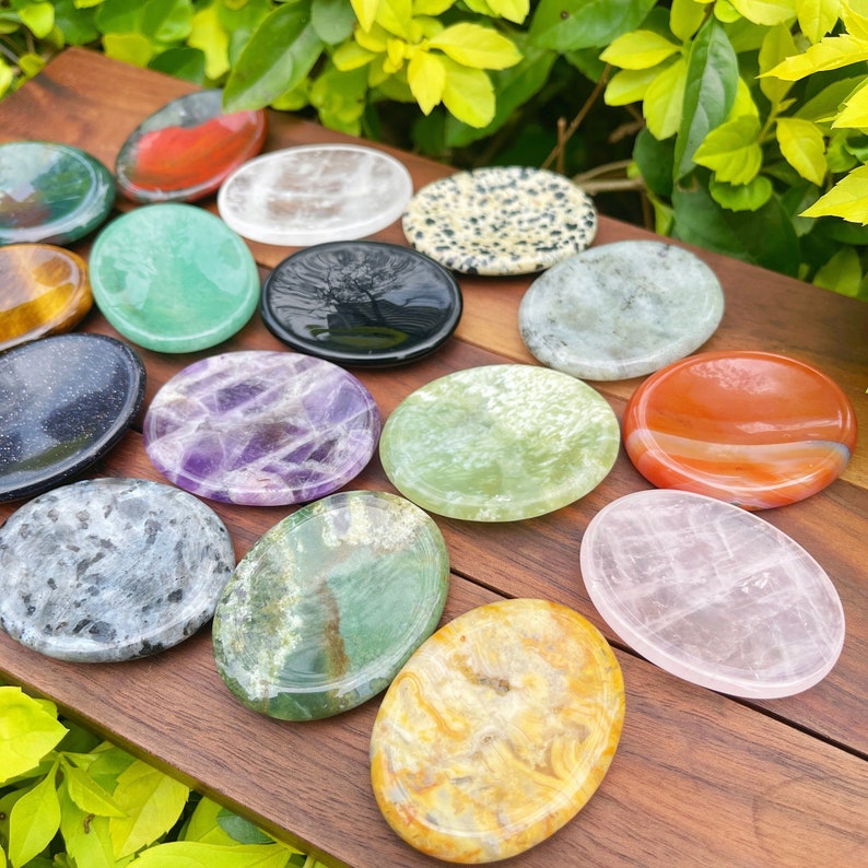 May include: Assortment of 15 polished gemstone coasters in various colors and patterns, including green, purple, red, black, white, and brown. The coasters are oval shaped and made of natural stone.
