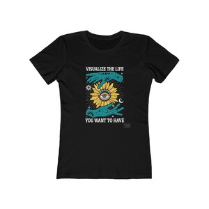May include: Black t-shirt with a graphic design featuring a sunflower with an eye in the center, held by two hands. The text "VISUALIZE THE LIFE YOU WANT TO HAVE" is printed above and below the graphic in white.