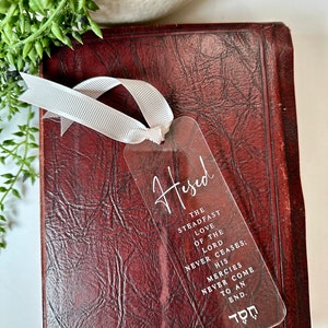 Peut inclure: Un marque-page en acrylique transparent avec le mot "Hesed" écrit en cursive. Le marque-page présente une citation sur l'amour indéfectible du Seigneur et ses miséricordes sans fin. Le mot hébreu pour "Hesed" est également inclus au bas du marque-page.