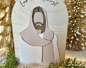 May include: A wooden cutout of Jesus with the words "Look Unto Christ" above him. The cutout is painted in shades of pink and brown.