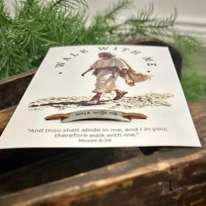 May include: A white card with the words "WALK WITH ME" and an illustration of a person walking. The card also features a quote from Moses 6:34. A small metal accent with the words "WALK WITH ME" is below the image.