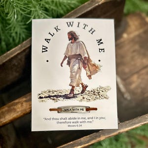 May include: A white card with the words "WALK WITH ME" arched above an image of a figure in white robes. Below, a small metal bar reads "WALK WITH ME". The card includes a quote from Moses 6:34.