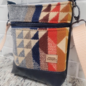 May include: A crossbody bag with a geometric pattern in shades of gray, beige, blue, and red. The bag has a navy blue base and a light pink strap. The text "Whatcha Making Now" is on a small tag.