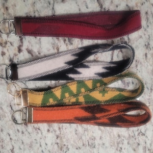 May include: Four different keychains with colorful patterns and a metal key ring. The keychains are made of fabric with a zig-zag stitch around the edges.