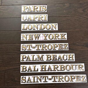 May include: Eight gold-colored vinyl stickers with the names of cities: Paris, Capri, London, New York, St-Tropez, Palm Beach, Bal Harbour, and Saint-Tropez.