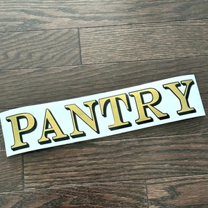 May include: Gold vinyl lettering spelling out the word "PANTRY" on a white background.