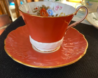 May include: A red teacup and saucer with a floral pattern and gold trim. The teacup has a white interior and a white band around the bottom.