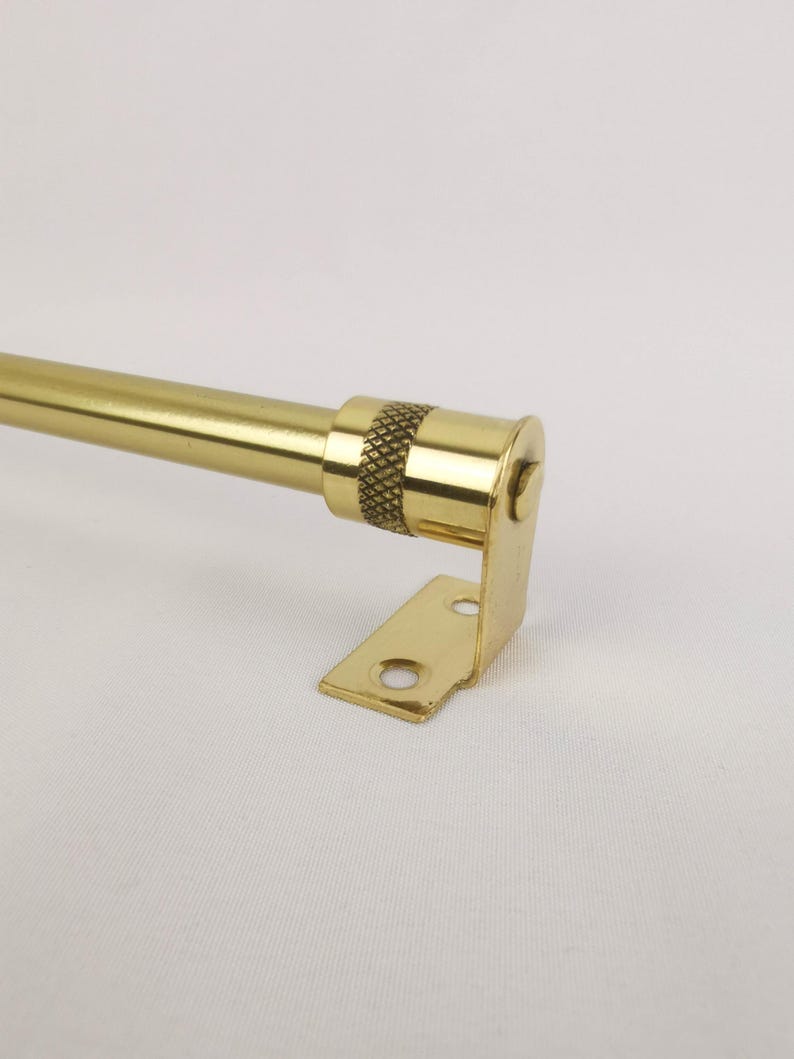 May include: A gold metal curtain rod with a decorative finial and a bracket. The rod is approximately 2.5 cm in diameter.