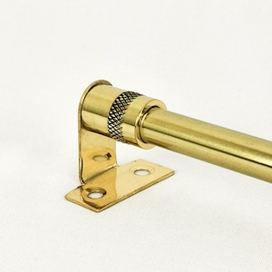 May include: A gold metal curtain rod with a decorative knob and a bracket. The rod is attached to the bracket with two screws.