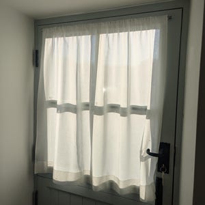 May include: A white sheer curtain hangs in a window with a light grey door. The door has a black handle and a key in the lock.