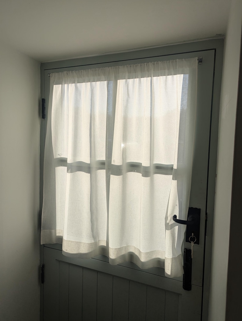 May include: A white sheer curtain hangs in a window with a light grey door. The door has a black handle and a key in the lock.