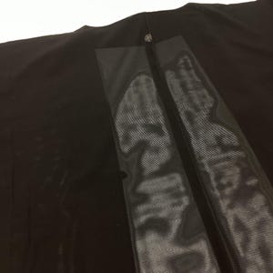 May include: A black garment featuring a central vertical panel with a semi-sheer, ribbed texture. The fabric is solid black on the sides, transitioning into a distinct, vertically striped, translucent section that runs down the middle of the piece.