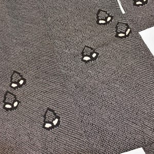 Puede incluir: Tela gris oscuro con un patrón repetitivo de pequeños círculos y formas geométricas negras y blancas dispersas. La tela está cortada en una prenda de estilo kimono con un forro blanco visible en los bordes.