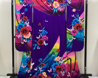 May include: A purple kimono with a striking floral and butterfly pattern. The design incorporates a rainbow gradient. The kimono is displayed on a black stand. The flowers are red, blue, and yellow. The garment is a traditional Japanese robe.