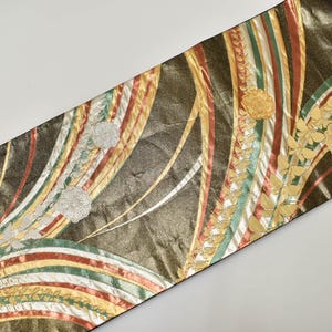 Può includere: Tessuto decorativo con sfondo marrone scuro e strisce dorate, rosse, verdi e bianche. Il tessuto presenta ricami floreali dorati e argentati. Il design generale è un mix di colori e motivi.