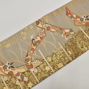 Può includere: Tessuto decorativo con un motivo ripetuto di farfalle stilizzate, fiori e forme geometriche. Il design presenta accenti dorati, arancioni, rossi e bianchi su sfondo grigio. Il tessuto ha un bordo floreale.