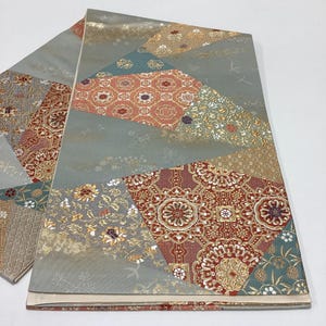 May include: A folded textile featuring a patchwork design of geometric and floral patterns in shades of red, gold, teal, and grey. The fabric displays intricate woven details with metallic accents and a smooth, satin-like finish throughout.