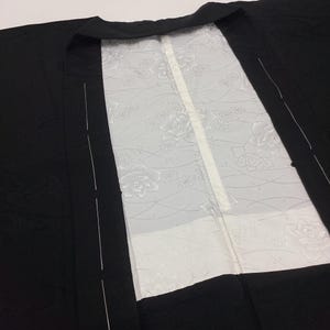 May include: A black garment featuring a wide collar and a contrasting white inner panel. The white section displays a subtle, tonal floral pattern with delicate line work, while the black outer fabric remains solid and plain in appearance.