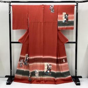 May include: A full-length, red kimono with decorative floral and geometric patterns. The kimono features a gradient design with bands of white, gray, and black. The sleeves are wide, and the garment is displayed on a black stand.