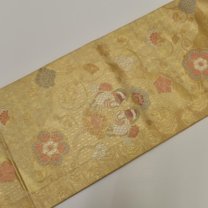 Puede incluir: Tela dorada con un intrincado diseño floral. El diseño presenta flores estilizadas en tonos rojos, blancos y grises, sobre un fondo texturizado. La tela es probablemente para uso decorativo, como un camino de mesa o tela decorativa.