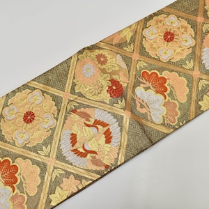 May include: A decorative textile with a repeating pattern of floral and bird motifs in a grid. The colors include gold, peach, red, and white. The textile is likely used for clothing or home decor.