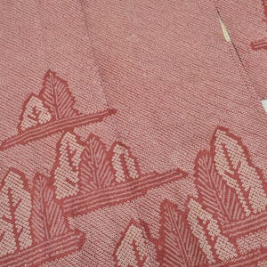 Puede incluir: Primer plano de un textil de color rosa polvoriento con un patrón repetido de formas de hojas estilizadas en un tono rosa más claro. La tela parece ser un kimono o una prenda similar.