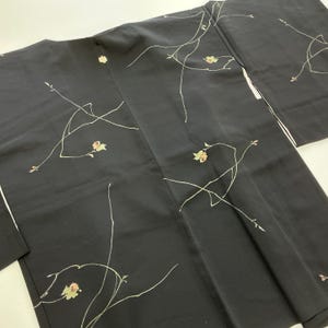 Könnte beinhalten: Schwarzer Kimono mit floralem Design. Der Kimono hat ein zartes Muster aus dünnen, cremefarbenen Linien und kleinen, mehrfarbigen Blumen. Das Kleidungsstück hat einen weißen Besatz an den Kanten.