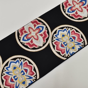May include: Black fabric with a repeating pattern of floral medallions. Each medallion features a central flower design in red, blue, and white, surrounded by a gold-colored border. The background is black.